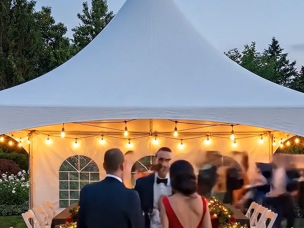 A tented dinner at dusk with string lights glowing over a long garland-decorated table.